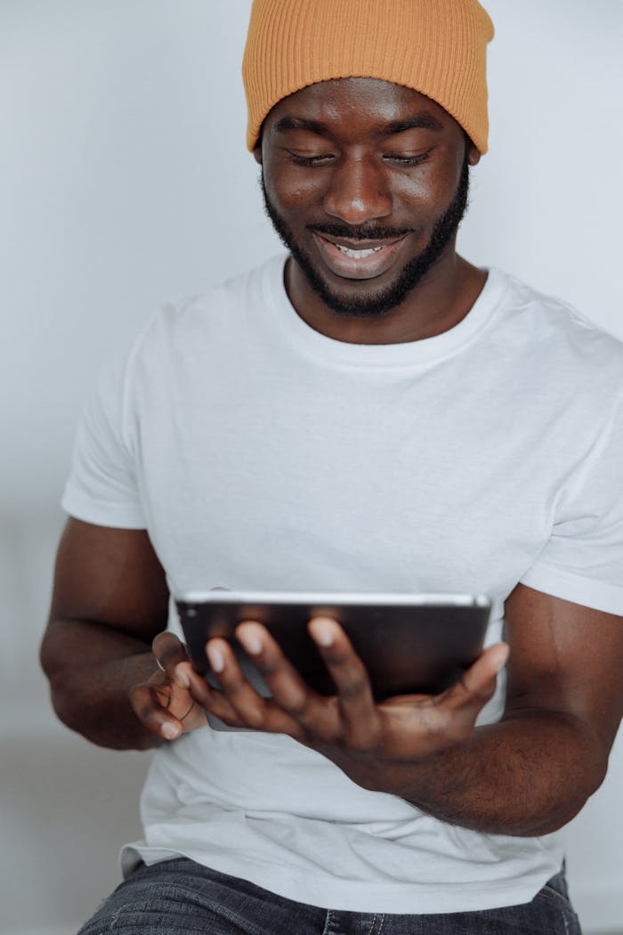 services-01 A smiling young man in a casual outfit using a tablet indoors for work or leisure.